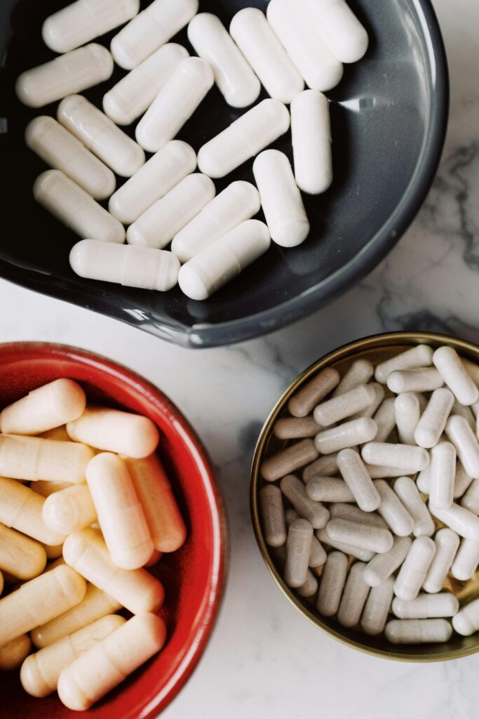 Top view of assorted white and beige capsules in colorful bowls placed on a marble surface, ideal for healthcare themes.