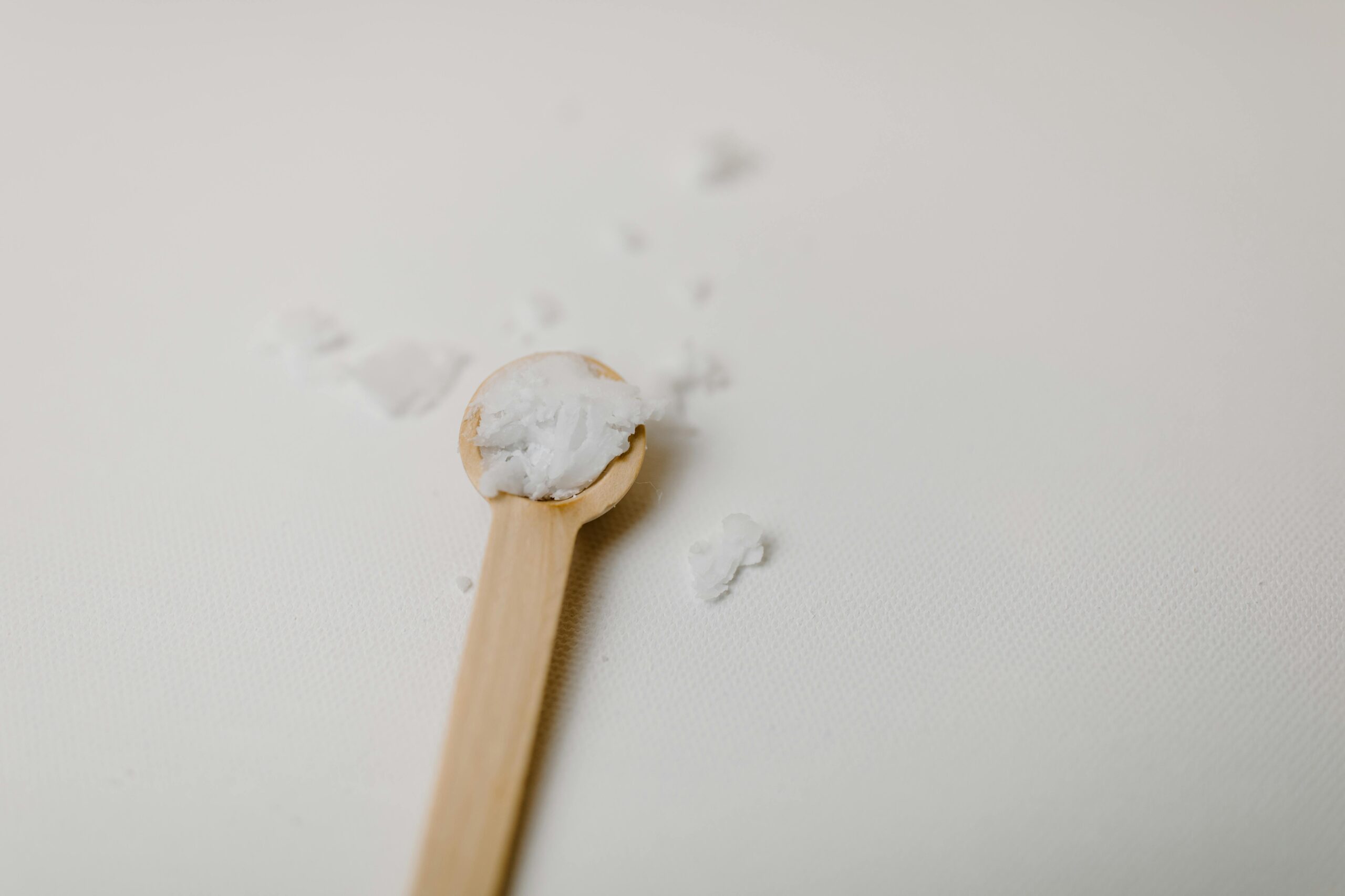Wooden spoon with scattered white bath salt on a textured surface, minimalist style.