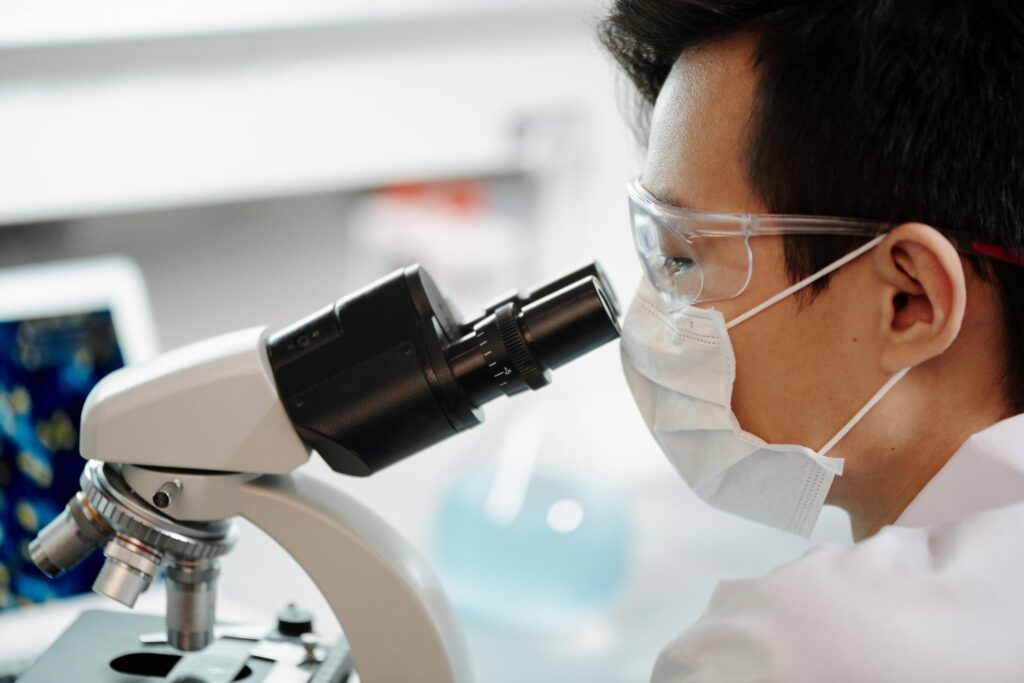 pexels-photo-4033151-4033151 Scientist wearing face mask and goggles examining samples through a microscope in a lab.