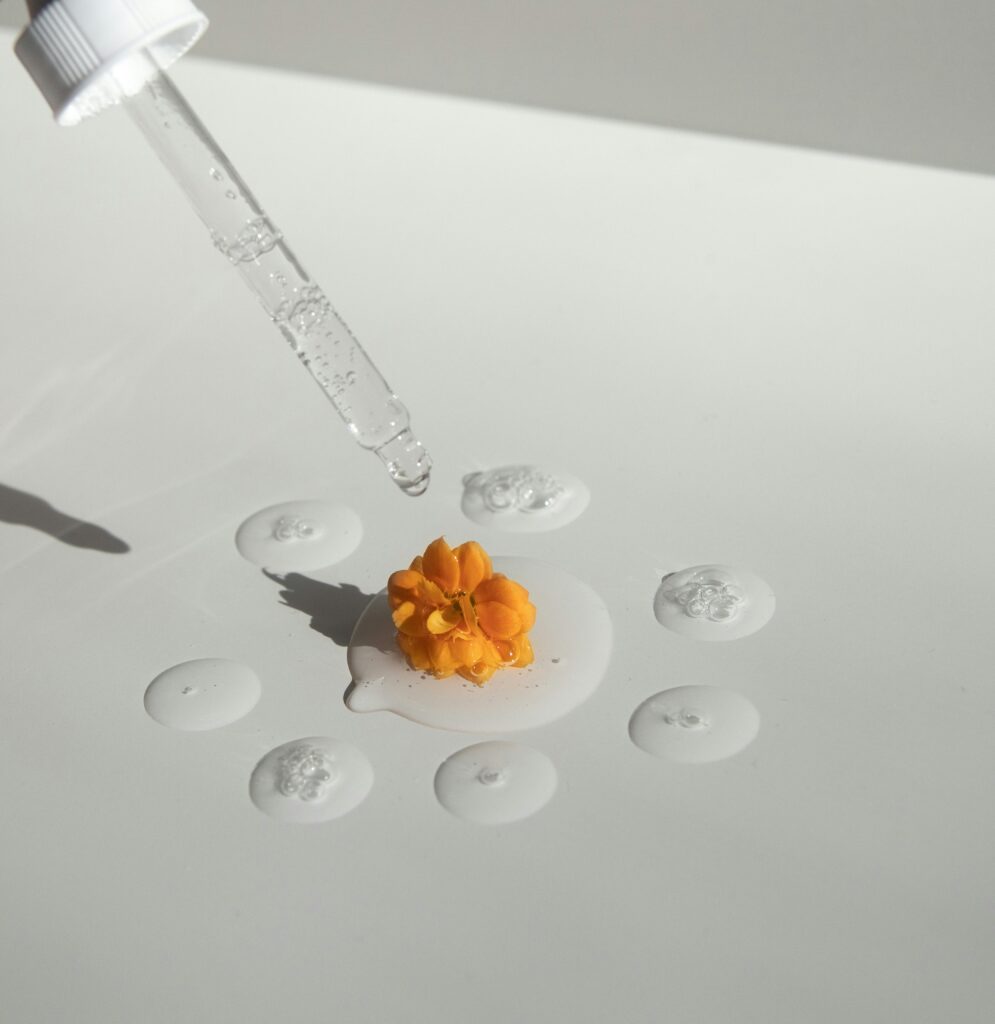 pexels-photo-6387848-6387848 From above of drops of transparent moisturizing cosmetic product dripped by pipette and small fresh flower head placed on white table