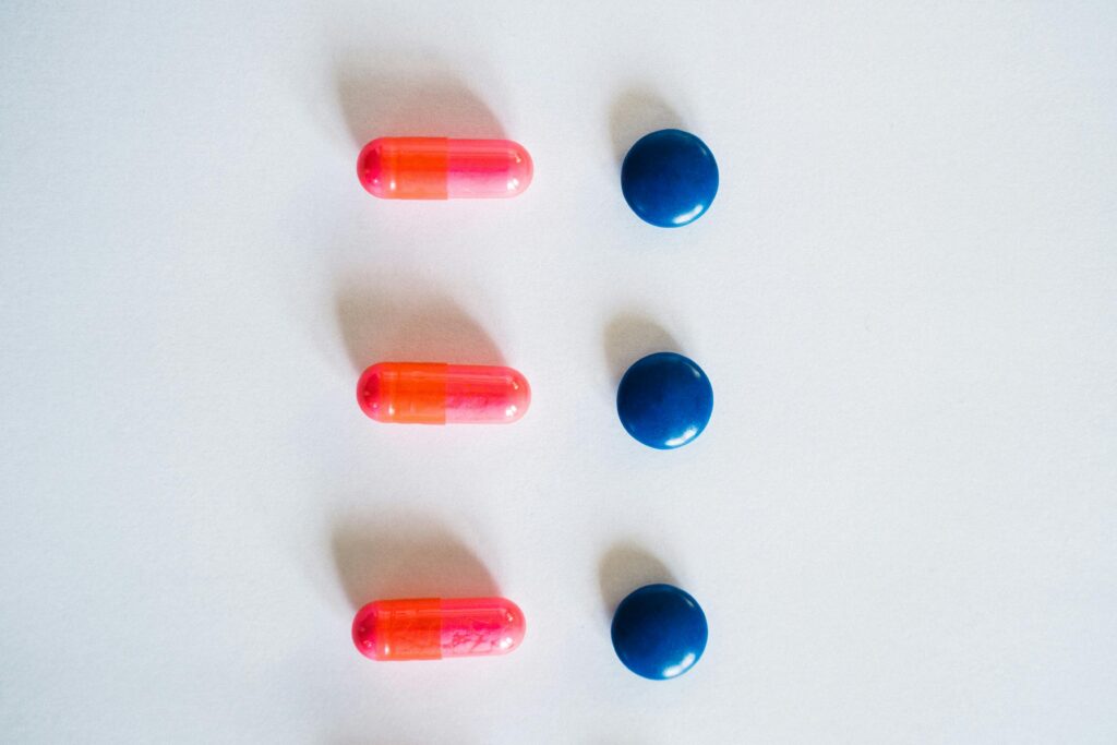 pexels-photo-7904440-7904440 Vibrant pink and blue medication capsules arranged on a clean white surface for healthcare concept.
